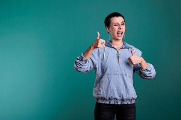 Positive confident woman doing thumbs up gesture in front of camera showing approval and agreement gesture with fingers in studio. Happy cheerful woman gesturing okay and positive symbol.