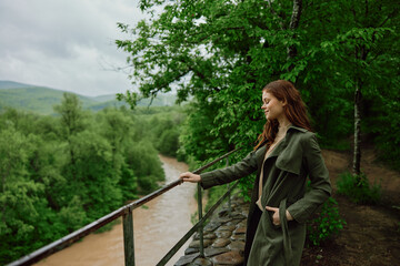 happy woman in a raincoat walks in the spring in the park near a stormy, mountain river