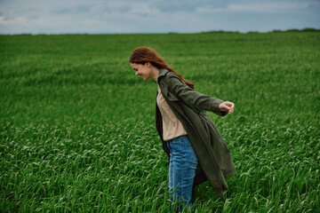 Naklejka na ściany i meble red-haired, happy woman stands in a green field in rainy weather. Emotions, harmony with nature