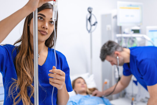 Young woman doctor anesthesiologist dressed in blue gown, puts the IV dropper in hospital room