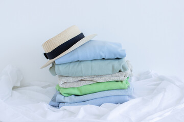Pile of clothes with straw hat on white, pastel color palette of stacked sweaters and jeans, fresh clothing folded for ironing