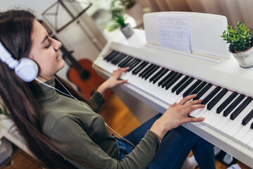 Happy girl is playing piano for her hobby relax time in home living room. Portrait Of Smiling Teenage Girl At Home Playing The Piano © Mediteraneo