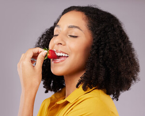 Woman, face and eating strawberry for natural nutrition, dieting or healthy food against a gray studio background. Happy female smiling and enjoying tasty organic fruit for health, diet or wellness