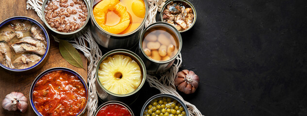 Canned vegetables, beans, fish and fruits in tin cans on black background. Food stocks.