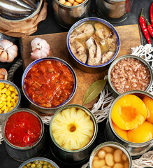 Canned vegetables, beans, fish and fruits in tin cans on black background. Food stocks.