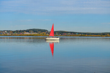 Fototapeta premium a white yacht with a red sail floats on the mirror surface of the lake