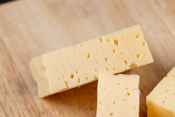 Hard cheese with holes cut into thick pieces on a cutting board