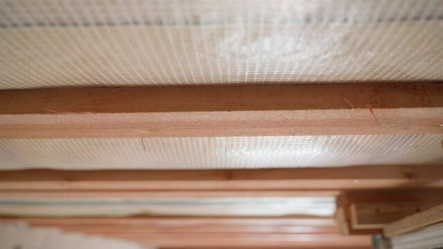 The roof of a private house is insulated with glass wool and closed with a vapor barrier, a wooden crate on the ceiling. Close-up, smooth camera movement