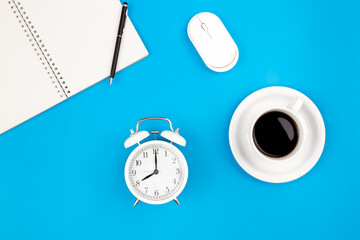 Alarm clock and coffee on blue background, work concept, flat lay.