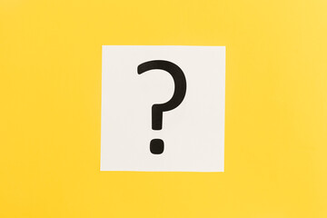 Question mark on white paper on yellow background, flat lay.