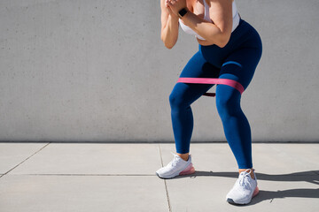 Woman exercising outdoors with resistance band around thighs - obrazy, fototapety, plakaty