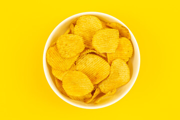 Close-up, a plate with potato chips on a yellow background, top view.