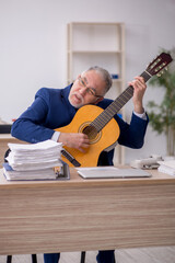 Obraz premium Old male employee playing guitar at workplace