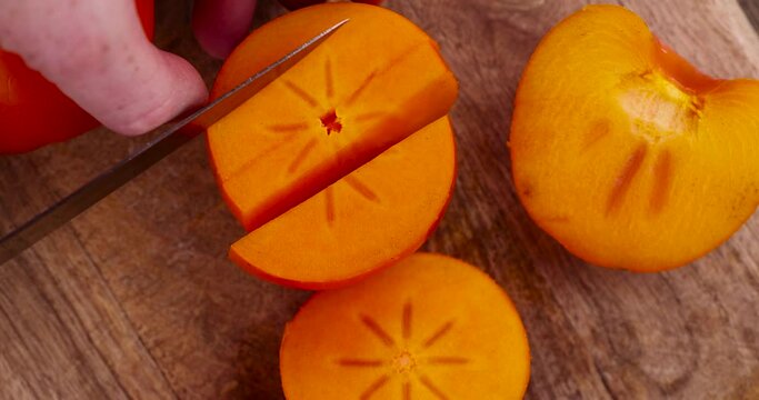 Half-ripe orange persimmon, fresh ripe persimmon cut into pieces on a cutting board with a sharp knife