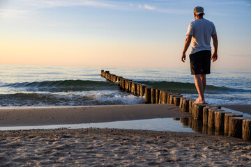Person balanciert auf Buhnen am Strand der Ostsee - obrazy, fototapety, plakaty