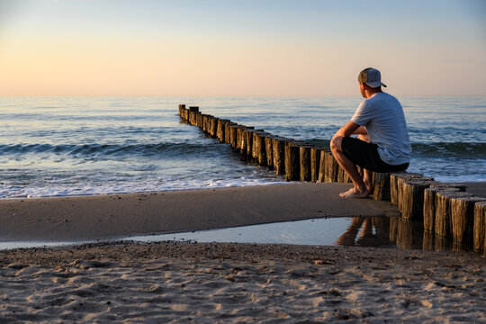 Mann sitzt auf Buhnen am Strand der Ostsee