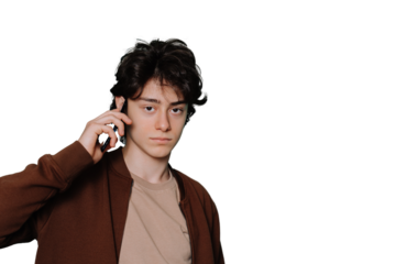 Confident brunette teen makes call using phone looks at camera against transparent background. Mockup, puzzled boy holds smartphone, handsome kid in casual calling.