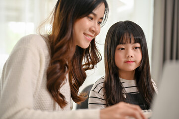 Kind Asian sister helping her little sister with online learning on laptop at home.