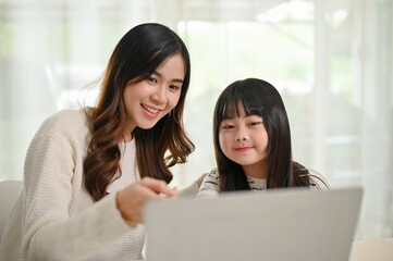 Kind and caring Asian sister helping her little sister with online study class on laptop