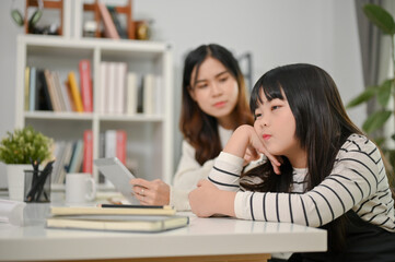 Obraz premium Lazy and bored young Asian girl sits at a table with her hand on her chin