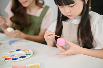 Close-up image, An adorable young Asian girl focuses on painting an Easter egg