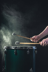 A man plays a musical percussion instrument with sticks on a dark background.