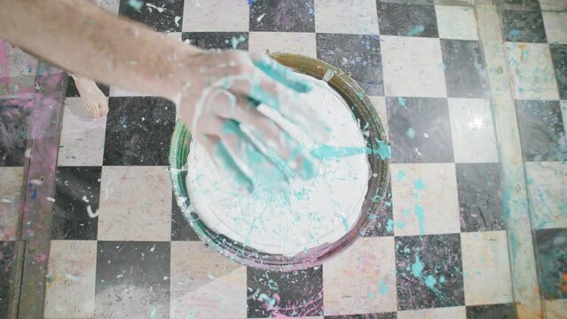 A hand hits a bass drum that is filled with white and blue paint and it all splashes up towards the camera in slow motion.