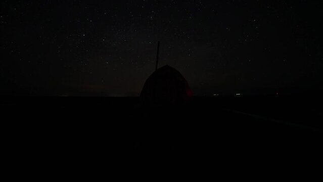 Timelapse of the starry night sky and the tent. Tourists go to bed. Planes, satellites and meteorites are flying in the sky. There is smoke from the chimney of the stove. The earth is flying.