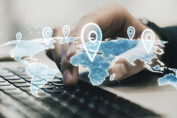 Close up of male hand using laptop keyboard on desktop with glowing and with location pins on blurry background. GPS and navigation concept.