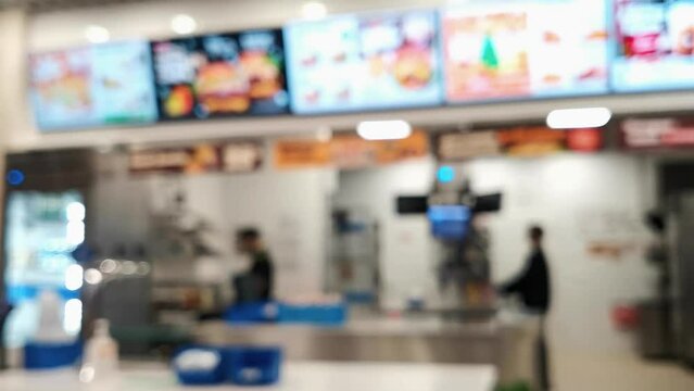 In blur, a trade workers at a fast food making a food at kitchen behind the cash register. Restaurant business at a food court in a shopping center. Unrecognizable place of sale of food.
