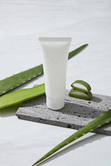 Mockup scene for cosmetic with white plastic tube unlabeled placed on gray stone and fresh aloe...