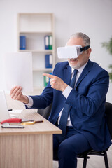 Old male employee wearing virtual glasses at workplace