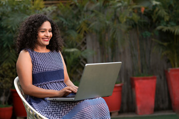 Indian woman sitting outdoor and using laptop.