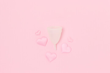 White menstrual cup and hearts confetti on a pink background. Minimal composition.