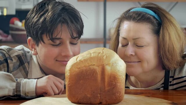 Mom and son breathe in the aroma of homemade bread and smile. Home cooking. Family values and pastime