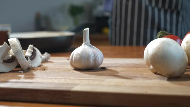 Slow motion. A man puts a head of garlic next to chopped and whole mushrooms. Culinary footage. Close up hand with garlic