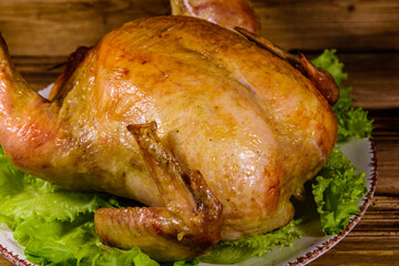 Plate with roasted whole chicken and lettuce leaves on a wooden table