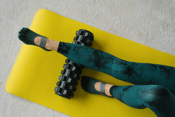 Close-up of the legs of a woman performing a myofascial release with a roller or roll on a gym mat...