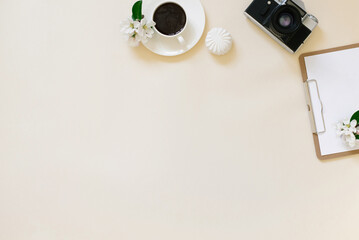 Vintage retro camera and white apple blossoms with a clean tablet and pen, a cup of coffee on a beige background. Feminine blogger flat lay. top view from copy space. Spring concept layout.
