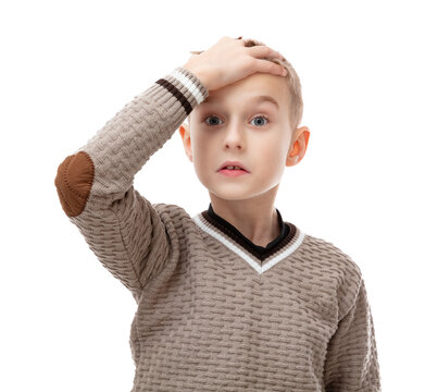 Upset little schoolboy looking at camera touching his head with shock impression, isolated on white background. Shocked eight year old chield in brown sweater posing in studio.