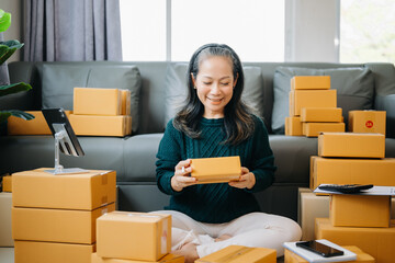 Fototapeta na wymiar Startup small business SME, Senior woman hand using smartphone or tablet taking receive and checking online purchase shopping order to preparing pack product box. business online shopping concept
