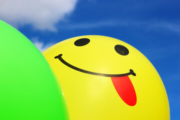 Two balloons against the sky. Yellow balloon shows the tongue. Fun, happiness, smiles, winks.