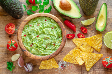 Guacamole, guacamole ingredients and chips on wooden background.  Flat lay.