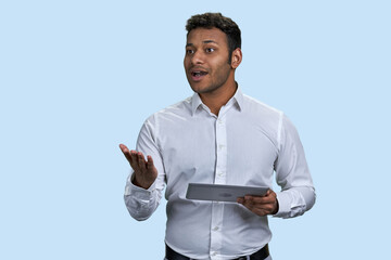 Speech of a young southeast indian man with tablet pc. Isolated on pastel blue background.