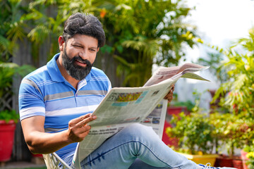 Indian man sitting outdoor and reading news paper.