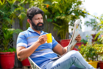 Indian man drinking tea or coffee and reading news paper