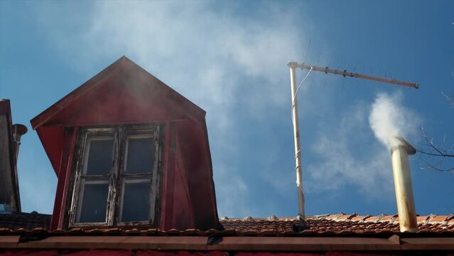 View of the roof of the house, the window and the chimney from which the smoke comes.