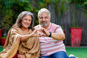Indian senior couple smiling and making heart shape with hand. - Powered by Adobe