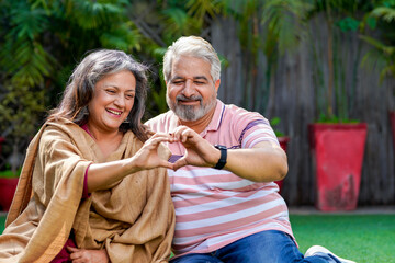 Indian senior couple smiling and making heart shape with hand.