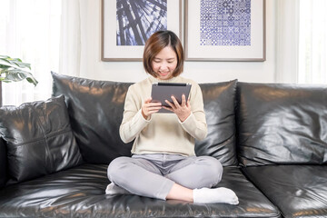 Happy relaxed young woman sitting on the sofa using a mobile phone Smiling woman laughing holding a smartphone looking at mobile phones enjoying online e-commerce shopping in mobile apps or watching v